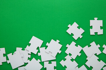 Fototapeta na wymiar Unfinished white jigsaw puzzle pieces on green background