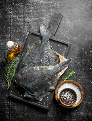 Raw fish flounder on a cutting Board with rosemary and spices.