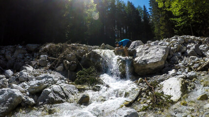 A man drinking water from a cascading waterfall in Hochturm region, Austrian Alps. The riverbed is...