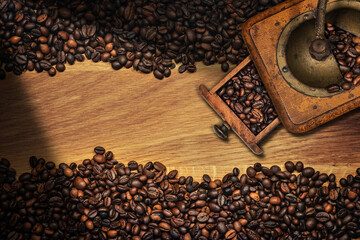 Large group of roasted coffee beans and a manual coffee grinder on a wooden background with copy...