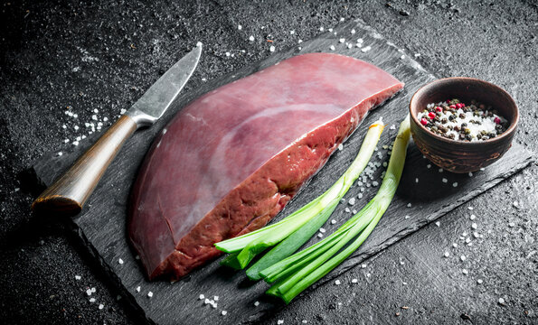 Raw liver on a stone Board with green onions and spices.