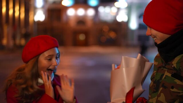 Portrait of teenage Caucasian boy waiting for girl tapping shoulder waving greeting. Happy loving Caucasian teen couple meeting on night city street dating on Valentine's
