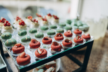 Candy bar. White wedding cake decorated by flowers standing of festive table with deserts, strawberry tartlet and cupcakes. Wedding. Reception Tartlets