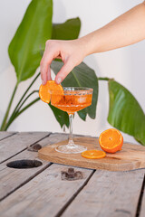 Cocktail called Aperol spritz and gin tonic or orange drink spritz with ice..Sok drink pomarańczowy z ręką. Ręka nakłada pomarańczę. Egzotyczny drink, egzotyczne zielone liście w tle.  © Julia