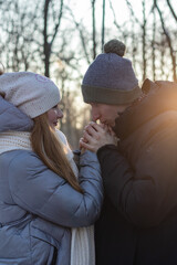 Careful young man warming his girlfriend hands in winter park