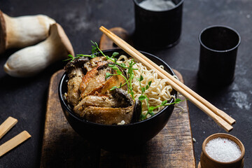 Noodles with eringi mushrooms in a black plate