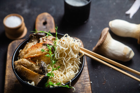 Noodles with eringi mushrooms in a black plate