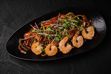 Stir-fried yakisoba noodle with vegetable and shrimps on black concrete background. Asian food style. Top view