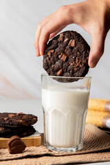 Chocolate cookies are dipped in a glass of milk