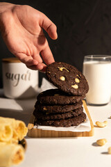 Lots of chocolate chip cookies on a stand with nuts and milk. A hand is holding a chocolate chip cookie