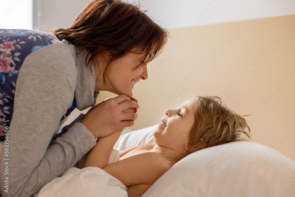 Wall mural Mother and child, blond toddler boy, cuddling in bed in the morning, love and tenderness