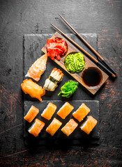 Philadelphia roll and various sushi with sauce on a stone Board.