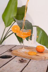 Sok drink pomarańczowy plusk. Nalewanie drinka, przygotowanie drinka. Szkło do drinka, kieliszek. Sok drink w kieliszku na nodze. Egzotyczny drink, egzotyczne zielone liście w tle. Cocktail Aperol. © Julia