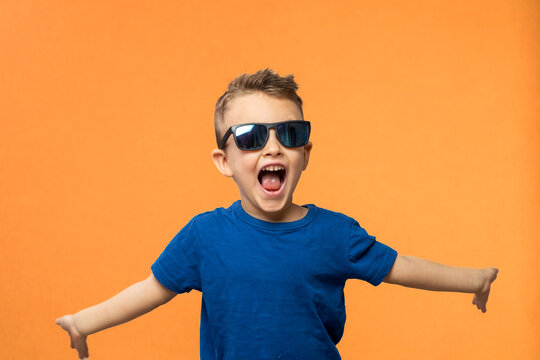 Portrait of surprised cute little toddler boy in sunglasses. Child with open mouth having fun isolated over orange background. Looking at camera. Wow funny face