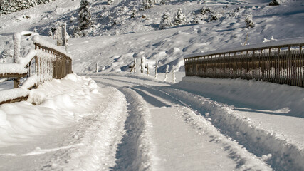 a car track in the fresh snow on a mountain road with a wood bridge at a sunny winter day