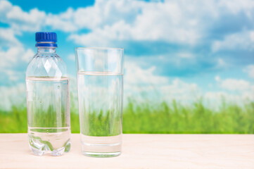 Plastic bottle and glass with pure water on grassland landscape background