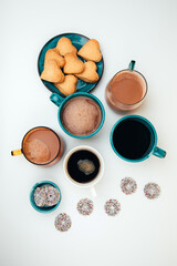 Mugs of coffee with foam and a plate with heart-shaped shortbread cookiesa and chocolate rounds on a white background. Tpo view