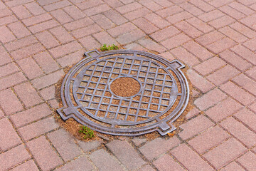 Iron sewer manhole on the ground among the tiles close-up