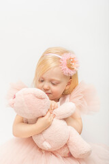 Pretty little girl hugs pink teddy bear. Blonde girl in lush pink dress and hoop decoration. White background. Vertical