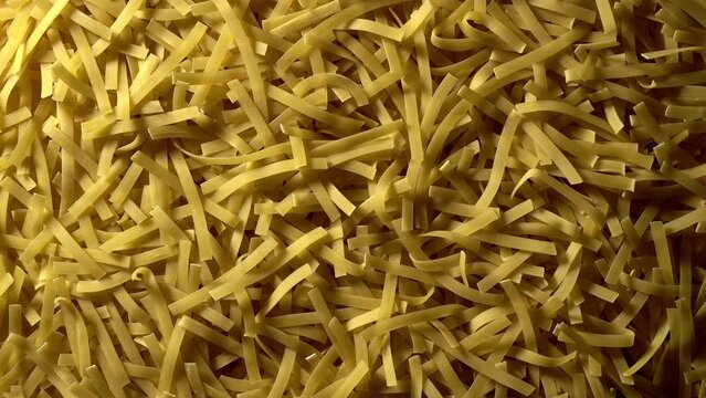 Uncooked Tagliatelle Lungo pasta rotating in slow motion - top view, flat lay, low key, food background. Raw dried organic golden long macaroni texture. Italian food, cuisine and culture close up
