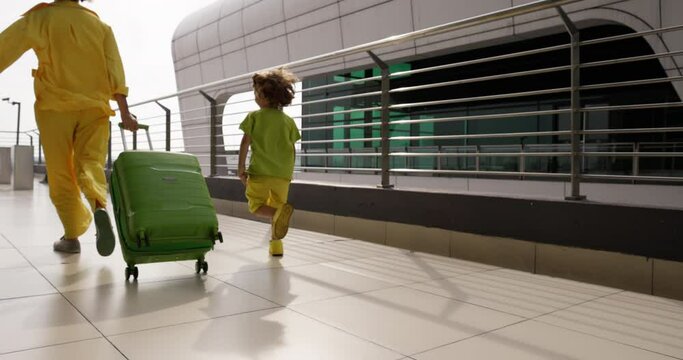 Backs of woman and child hurrying to their flight. Sister and brother rushing to their flight to fly home after long, happy vacation. Sister and brother in matching yellow, light green outfits running