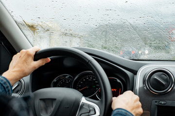 Senior woman driver driving her car on a rainy day. Elderly woman holding the steering wheel as she...