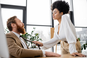 african american woman pulling tie while seducing bearded coworker with closed eyes.