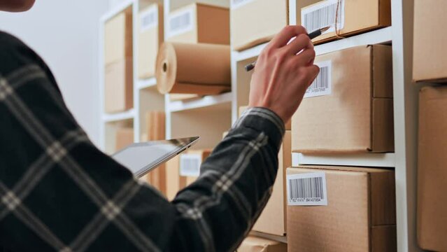The process of work of a storekeeper in a cargo warehouse warehouse worker holds a tablet in his hands against the background of boxes checks the sending parcels with an online database. Sending boxes