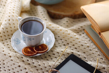 Vintage books, reading glasses, e-reader, cup of tea, bowl of biscuits and lit candle on the table. Selective focus.
