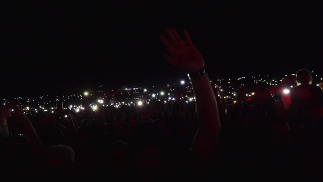 Dark background with concert crowd waving hands with mobile phone lights