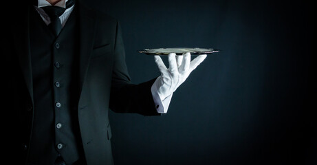 Portrait of Butler in Formal Attire and White Gloves Holding Silver Serving Tray on Black Background. Service Industry and Professional Hospitality - obrazy, fototapety, plakaty