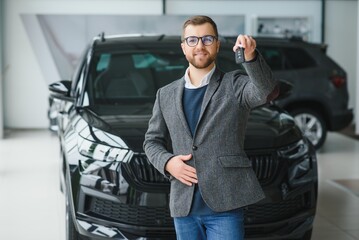 Happy owner of a new car. Emotional handsome man in casual clothes is happy, buying a car in the dealership.