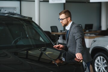 Visiting car dealership. Handsome bearded man is stroking his new car and smiling