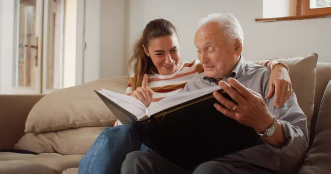 Portrait of a Nostalgic Woman Bringing the Family Photo Album to her Senior Father so They Can Watch Photos Together. Old Man Sharing Memories and Stories with his Daughter in a Bonding Moment