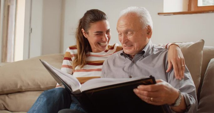 Portrait of a Nostalgic Woman Bringing the Family Photo Album to her Senior Father so They Can Watch Photos Together. Old Man Sharing Funny Memories and Stories with his Daughter 