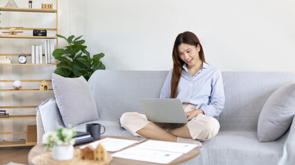 Woman using laptop to work or do homework at home with smiling face in her living room, Creating happiness at work with a smile, Live performance or video call with laptop, Work from home.