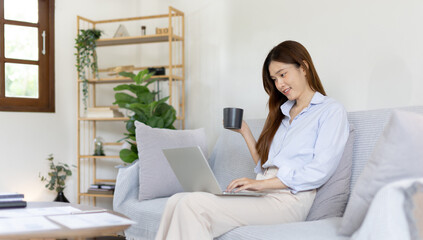 Woman using laptop to work or do homework at home with smiling face in her living room, Creating happiness at work with a smile, Live performance or video call with laptop, Work from home.