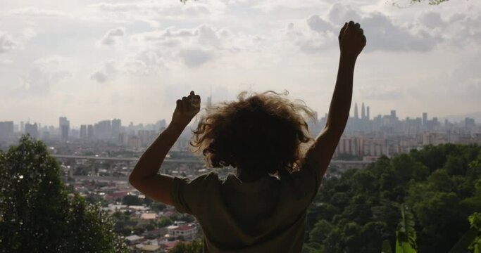 Happy and free from worries, woman dances with arms raised above head and rejoices in her journey to city of her dreams. A woman traveler has finally visited her beloved city and is enjoying scenery.