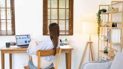 Beautiful young asian woman watching live video or video call of teacher teaching on laptop in her home, Take notes of important conversations and messages during the teacher's teaching.