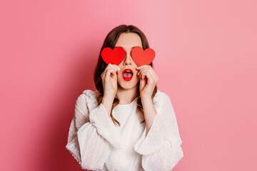surprised girl closes her eyes with paper hearts isolated on pink background. Valentine's day