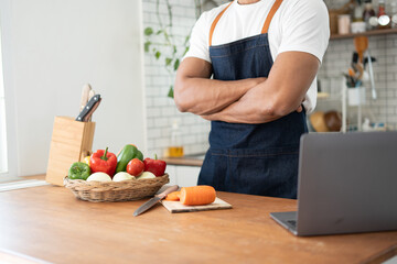Happy asian man preparing vegetable salad in kitchen.