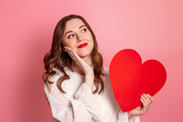 A dreamy girl in love holds a big red heart on a pink background. Valentine's day concept