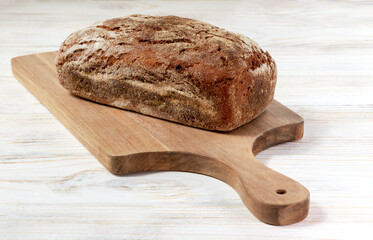 Freshly baked dark bread on a board on a white wooden background