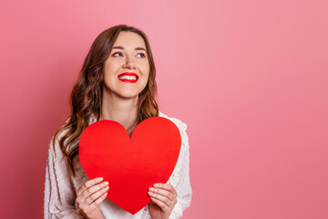 portrait of a girl holding big red heart card isolated on pink background