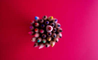 Red pencil standing out from others. Colorful wooden pencils on red background