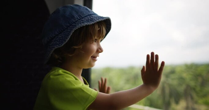 The happy child went on long journey by bus for the first time. Leaning his hands on the glass of the bus, the boy is excited about long journey on bus. The boy looks out window of bus with interest.