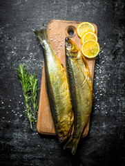 Smoked fish on a cutting Board with lemon and rosemary.
