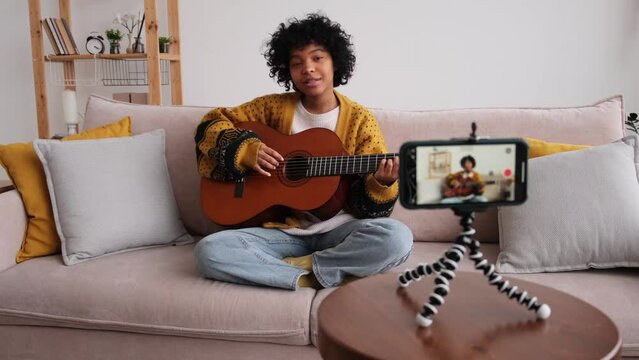 Blogger guitarist. Happy african american girl blogger playing guitar singing song recording vlog. Social media influencer woman streaming recording at home studio. Music content creator broadcast