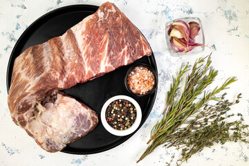 Raw pork ribs on a black plate with fragrant spices and herbs on white, top view of seasoned pork...