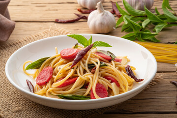 Stir fried Hot dog or sausage with Spaghetti with Dried Chili and garlic in white plate.Fusion food